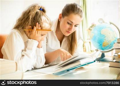 Young mother and daughter reading textbook while doing homework