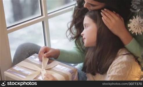 Young mother and daughter with Christmas gift box look in window