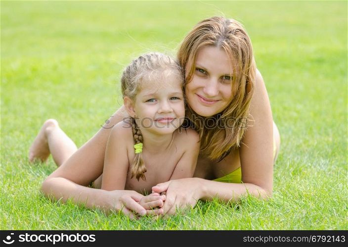 Young mother and five year old daughter hugging lying on green grass and looking to the frame