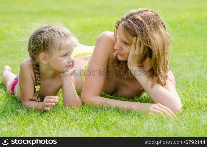 Young mother and five year old daughter lying on green grass and looking at each other