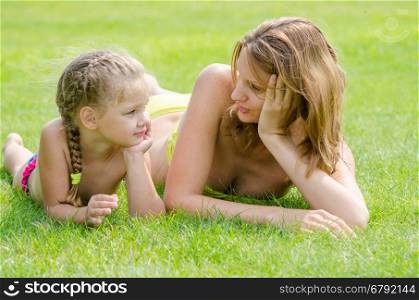 Young mother and five year old daughter lying on green grass and looking at each other