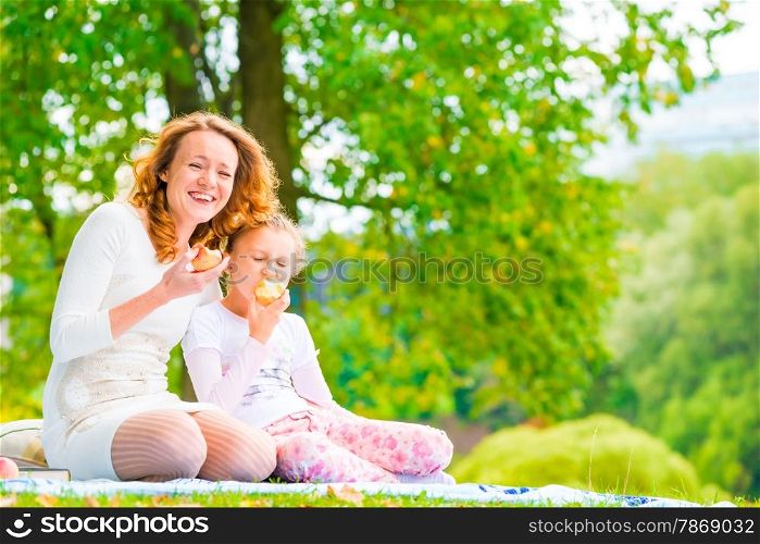 young mother and her daughter eating apples in the park