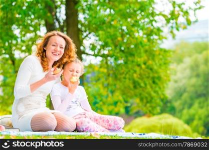 young mother and her daughter eating apples in the park
