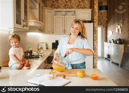 Young mother and her daughter mixing ingredients for cake in a bowl. Cute woman and little girl cooking on the kitchen, pastry preparation. Happy family prepares sweet dessert