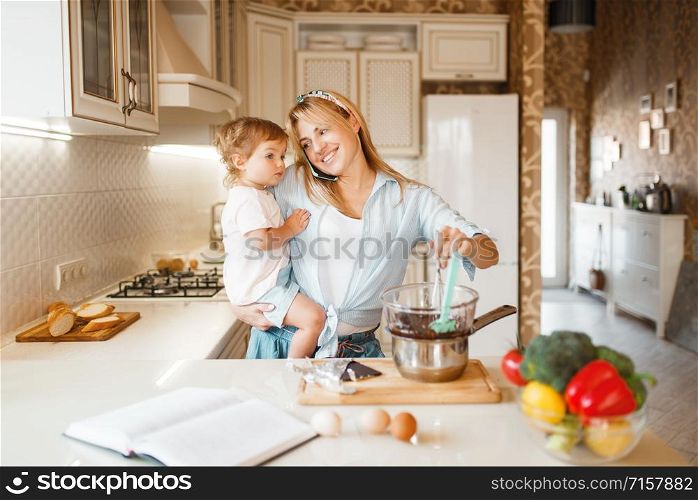 Young mother and her daughter prepares pastry with melted chocolate. Cute woman and little girl cooking on the kitchen. Happy family makes sweet dessert at the counter