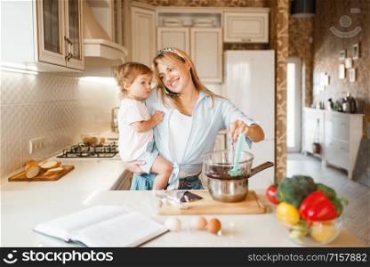 Young mother and her daughter prepares pastry with melted chocolate. Cute woman and little girl cooking on the kitchen. Happy family makes sweet dessert at the counter