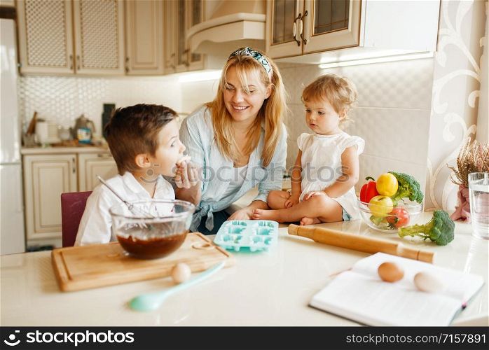 Young mother and her kids tastes fresh pastry with melted chocolate. Woman and little children cooking on the kitchen, cake preparation. Happy family eats sweet dessert