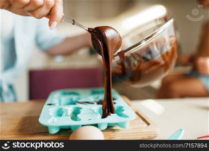 Young mother and kid fill melted chocolate in the baking form, closeup. Woman and little girl cooking on the kitchen, cake preparation. Happy family makes sweet dessert at the counter