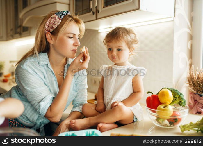 Young mother and kid tastes fresh chocolate pastry. Woman and little girl cooking on the kitchen, cake tasting. Happy family eats sweet dessert