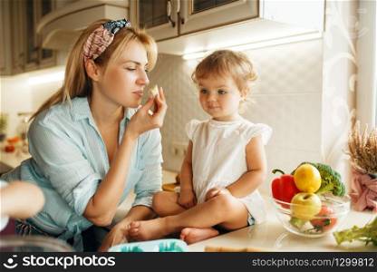 Young mother and kid tastes fresh chocolate pastry. Woman and little girl cooking on the kitchen, cake tasting. Happy family eats sweet dessert