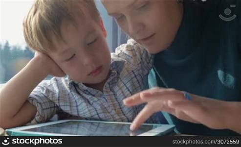 Young mother and little child entertaining with digital tablet in train. They playing game in turns. Family travel
