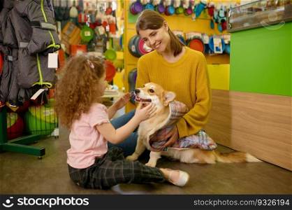 Young mother and little daughter choosing blanket for their corgi dog at pet shop. Happy family spending time together at supermarket for domestic animal. Young mother and little daughter choosing blanket for their dog at pet shop