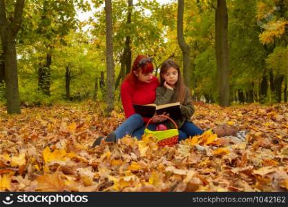 young mother and little daughters in bright sweaters on a picnic in nature read a book together. mom and daughter picnic