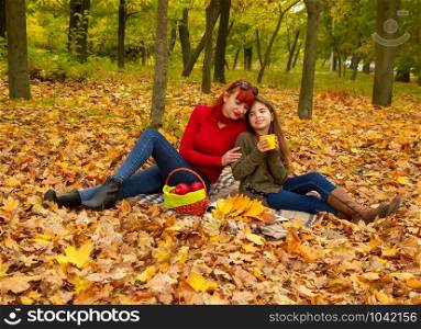 young mother and little daughters in bright sweaters on a picnic in nature drink tea. mom and daughter picnic