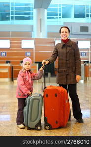 young mother and little girl with suitcases standing at airport