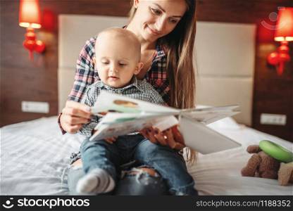 Young mother and little male child reading a book, kids education. Mom and son happy together at home, togetherness. Young mother and little male child reading a book
