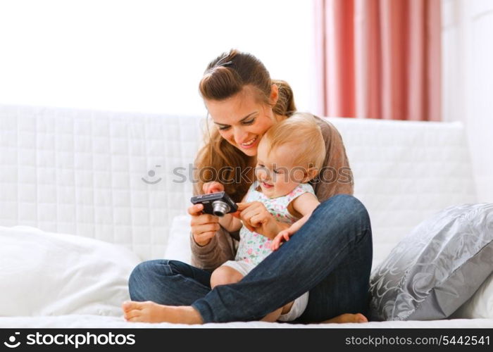 Young mother and smiling baby looking photos in camera at home&#xA;