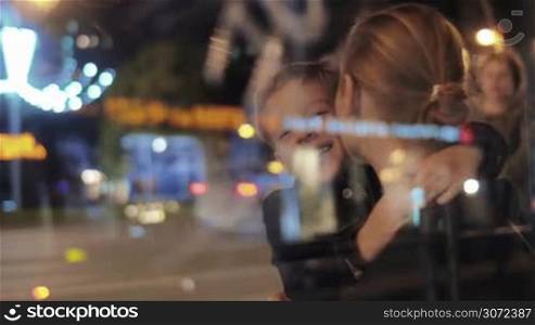 Young mother and son hugging and having fun in the evening city street. View through the glass