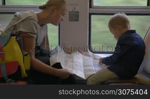 Young mother and son searching something together on map while traveling by train