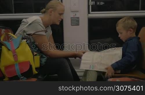Young mother and son traveling by train. They unfolding the map and looking at it
