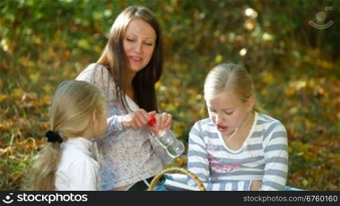 Young mother and two daughters enjoying autumn day at picnic in the park, children drinking water