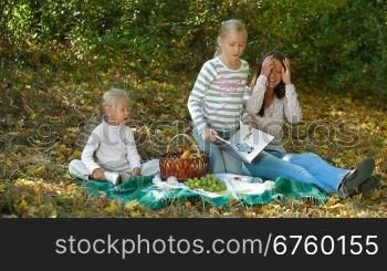 Young mother and two daughters enjoying autumn day at picnic in the park