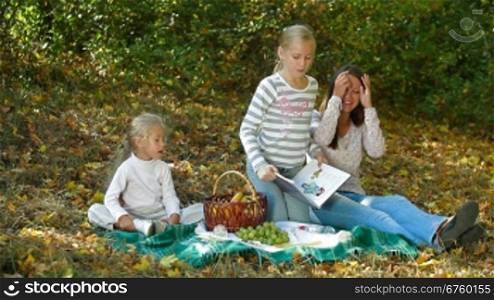 Young mother and two daughters enjoying autumn day at picnic in the park