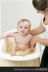 Young mother bathing her adorable baby in bathroom