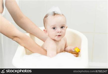 Young mother bathing her baby boy in plastic bath