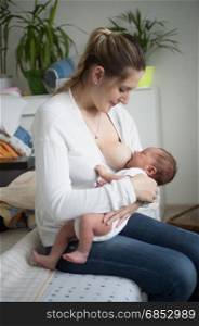 Young mother breastfeeding little baby in living room