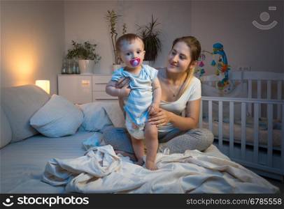 Young mother changing messy diapers to her baby boy on bed at night