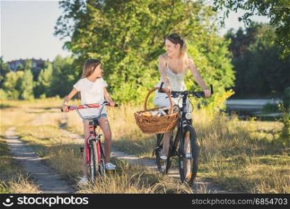 Young mother cycling with daughter riding to picnic