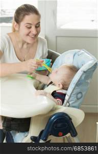 Young mother feeding baby boy in highchair