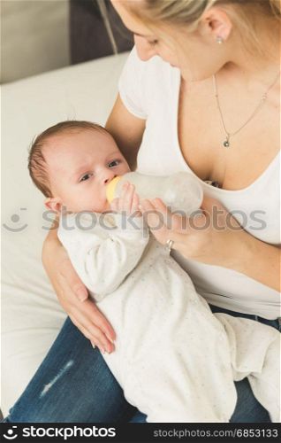 Young mother feeding her baby boy in bed from bottle