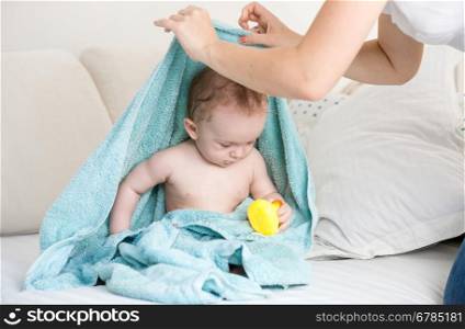 Young mother found her baby under blue towel playing with yellow rubber duck