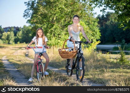 Young mother going to picnic with her daughter on bicycles