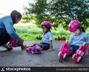 Young mother helps her daughter put on protective pads and a safety helmet before her roller skating practice on the park road. Active outdoor sport for kids.