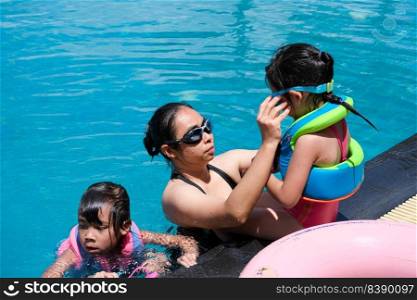 Young mother helps put on swimming goggles for her daughter before swimming. Happy family, mother and her daughter playing in the swimming pool. Summer lifestyle concept.