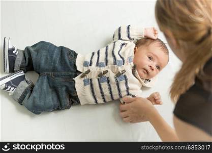 Young mother holding little baby son hand lying on bed