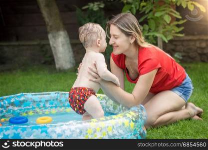 Young mother hugging her baby boy in swimming pool at garden