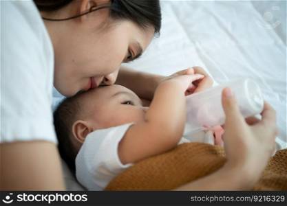Young mother hugging her newborn child to lull the baby to sleep while drinking milk In the white bedroom, warm sunlight in the evening of the day.