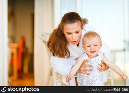 Young mother in bathrobe telling something to her adorable baby&#xA;
