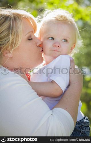 Young Mother Kissing and Holding Her Adorable Baby Boy in the Park.