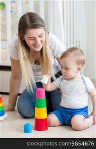 Young mother kissing her baby boy playing on on floor with colorful blocks