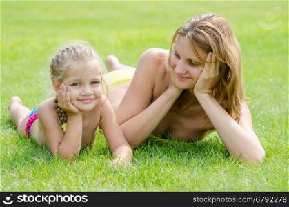 Young mother lying on green grass and looking at his five-year daughter who is lying near