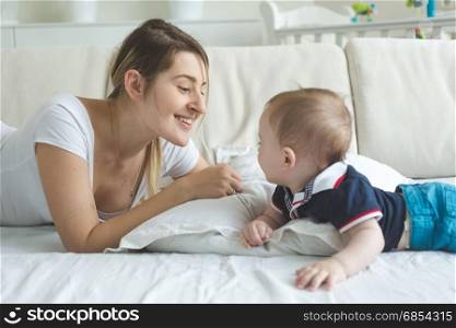 Young mother lying with baby boy on bed and looking at each other