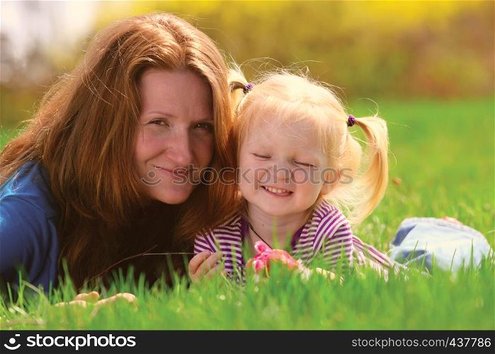 young mother lying with child girl on a grass at the park