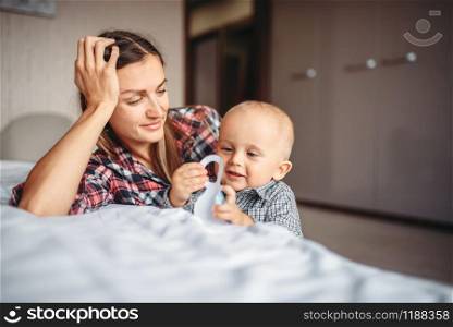 Young mother playing on bed with little male child. Mom and son happy together at home, togetherness