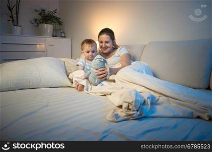 Young mother playing with her baby at night with doll