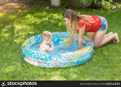 Young mother playing with her baby boy in outdoor swimming pool